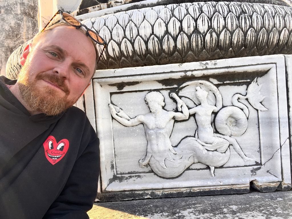 Eric Nielson beside a marble relief of two mermen at the temple of Apollo in Didyma, Turkey