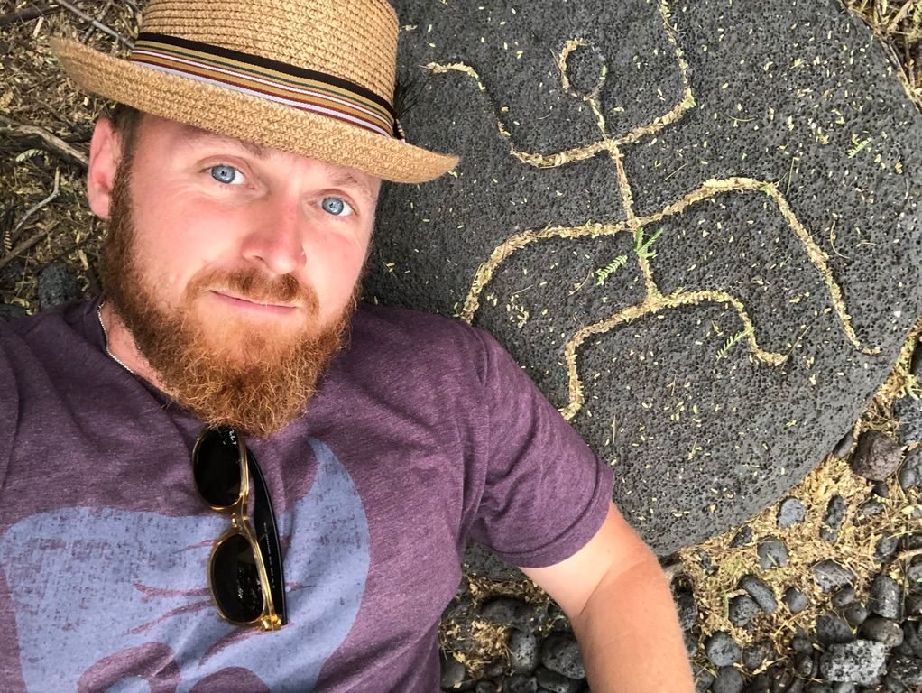 Eric Nielson in a straw hat beside ancient Hawaiian petroglyphs on the Big Island