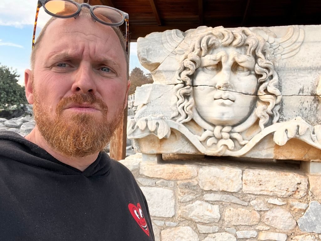 Eric Nielson frowning beside the carved Medusa head at Didyma, Turkey