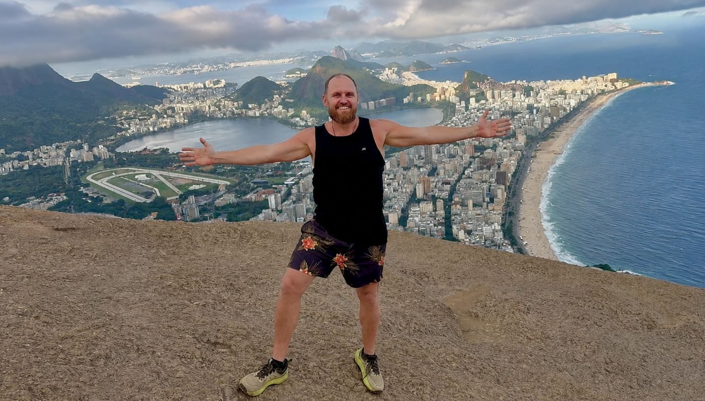 Eric Nielson, arms open above Rio de Janeiro with Ipanema beach behind him