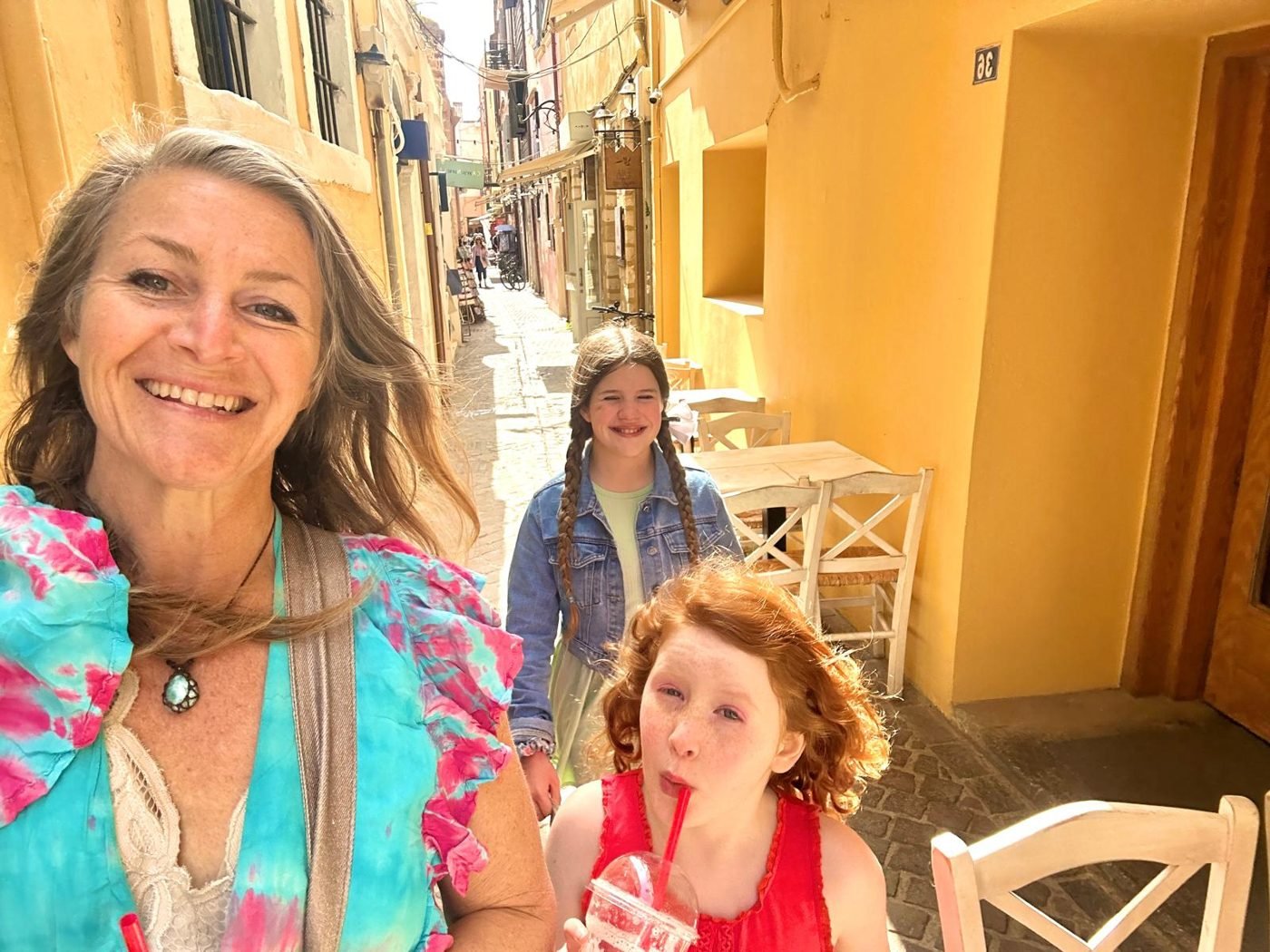Maya Lila Di Vento and her daughters walking a narrow yellow-walled lane in Crete, Greece