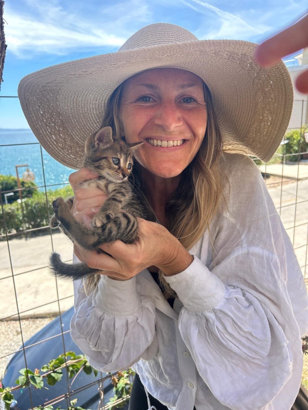 Maya Lila Di Vento in a wide straw hat holding a tabby kitten in Sarandë, Albania